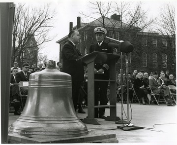 West Virginia University President James G. Harlow (left) and Naval Reserve Captain Marlyn E. Lugar are shown at dedication ceremonies for the bell from the armored cruiser and battleship U.S.S. West Virginia. In the background is Woodburn Hall and Chitwood Hall.