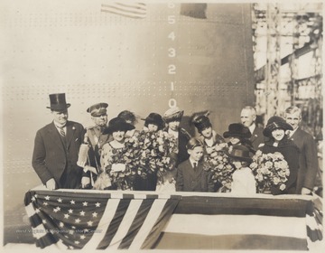 Miss Alice Wright-Mann, third from left holding a large bouquet and bottle, poses with a group on the battleship. The rest of the subjects are unidentified.Alice Wright-Mann, of Mercer County, sponsored the battleship which was built by the Newport News Shipbuilding and Drydock Co. of Newport News, Va. Wright-Mann was the daughter of a millionaire coalmine operator, Isaac T. Mann.