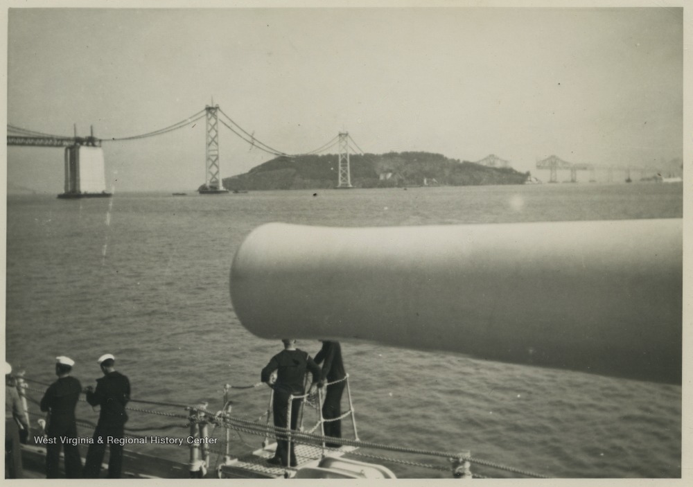 Sailors idle beneath the ship's gun barrel while passing the bridge. 