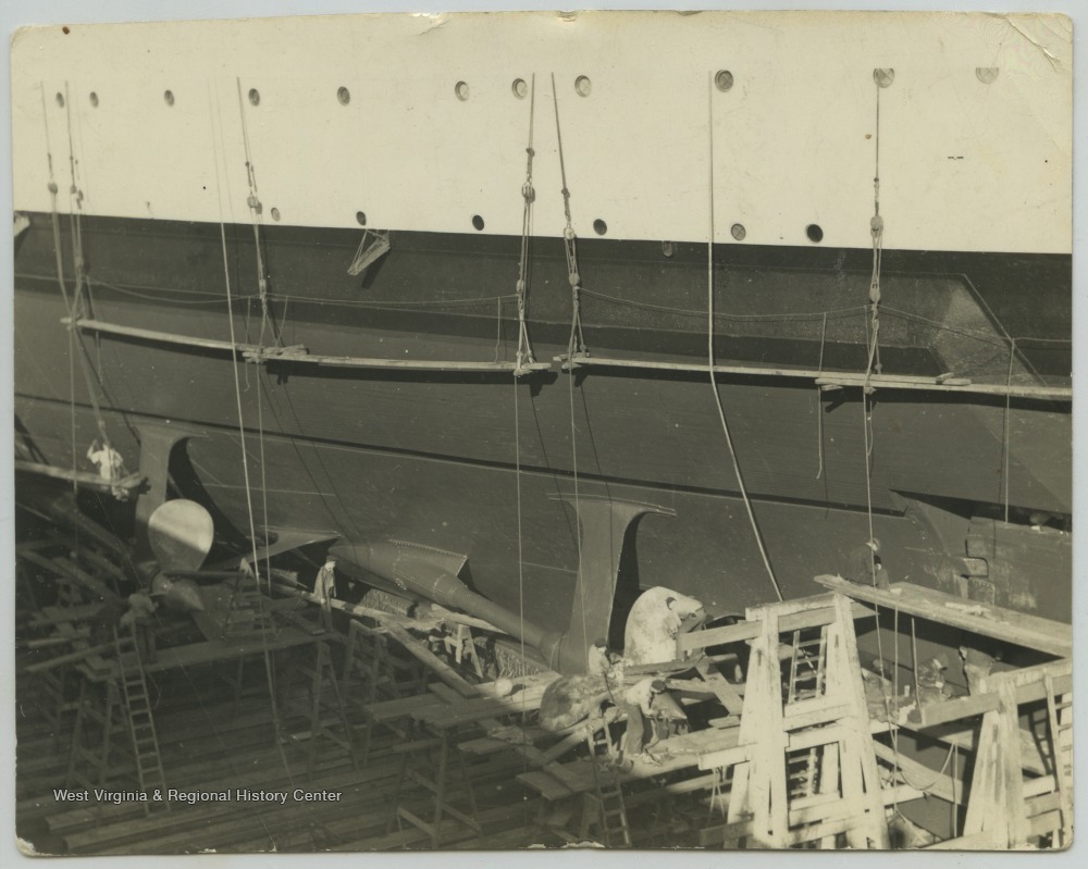 A group of men are scattered along the dry dock inspecting and repairing the ship. 